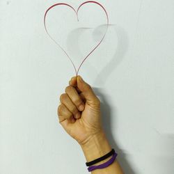 Close-up of hand holding heart shape against white wall