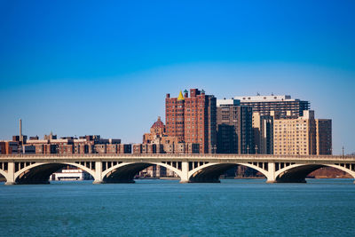 Bridge over river by buildings against blue sky