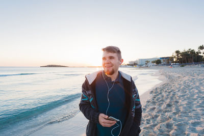 Portrait of young man standing on beach against clear sky