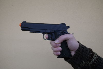 Close-up of hand holding handgun against wall