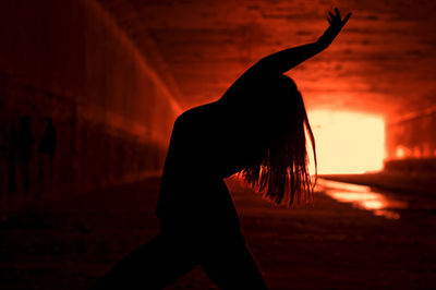 Silhouette young woman dancing under bridge during sunset