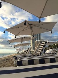 Parasols with lounge chairs at beach against sky