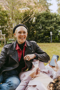 Portrait of happy gay woman wearing leather jacket while sitting with friend in back yard