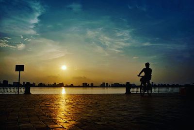 Silhouette man by sea against sky during sunset
