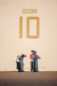 Full length of brothers standing against wall with text on it