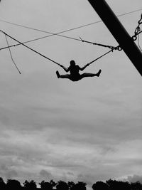 Low angle view of silhouette man climbing on rope against sky