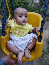 Cropped hand of man by girl sitting on swing