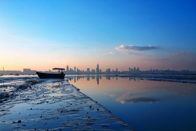 Boat at sea by cityscape against sky during sunset