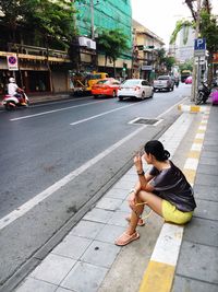 Woman showing peace sign while sitting on sidewalk in city