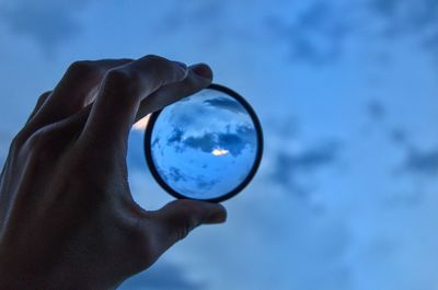 Close-up of hand holding glass against blue sky