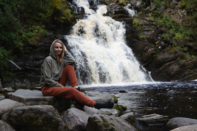 Portrait of woman sitting in waterfall in forest