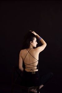 Portrait of young woman standing against black background