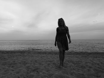 Portrait of woman walking at beach against cloudy sky