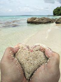 Cropped hands forming heart shape with wet sand at beach