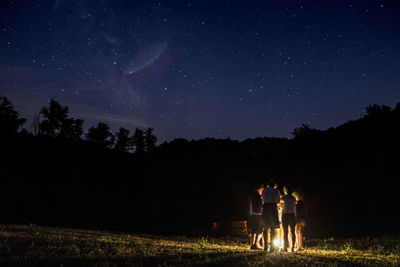 Rear view of people on field against sky at night