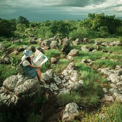 Rear view of woman sitting on rock against sky