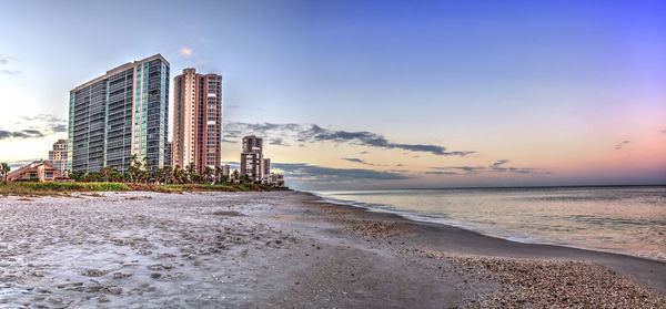 Sea by modern buildings against sky at sunset