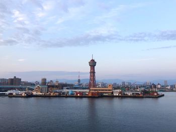 Buildings in city at waterfront against cloudy sky