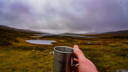 Cropped hand of man holding cup against landscape