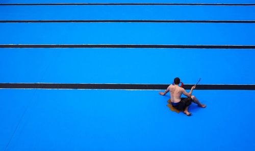 Rear view of shirtless man in swimming pool against clear blue sky