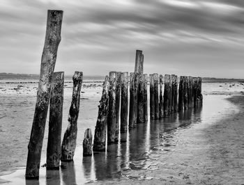 Wooden posts on beach against sky