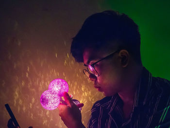 Close-up of young man looking at illuminated decoration in home