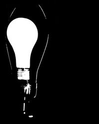 Illuminated light bulb over black background