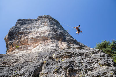 Low angle view of man rock climbing against clear blue sky
