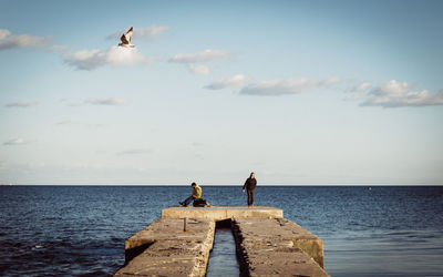 Man and woman on pier by sea against sky
