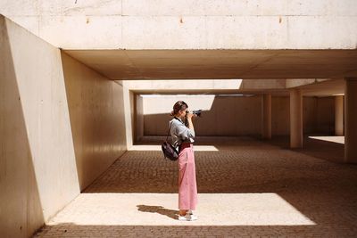 Side view of young woman photographing while standing in building