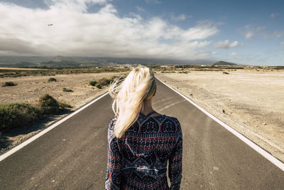 Rear view of woman standing on desert road against sky