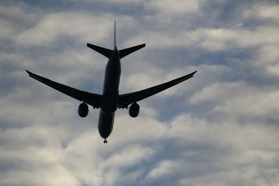 Low angle view of silhouette airplane flying against cloudy sky