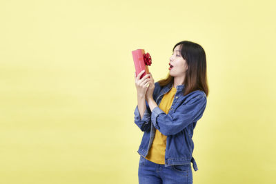 Full length of young woman standing against yellow background