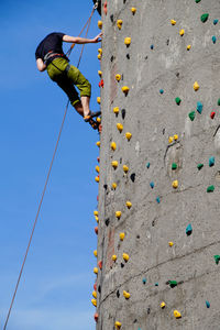 Low angle view of man climbing wall against sky