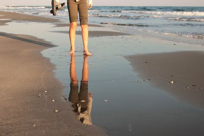 Low section of woman reflecting on water at beach