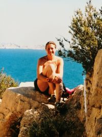 Portrait of smiling young woman sitting on beach against clear sky