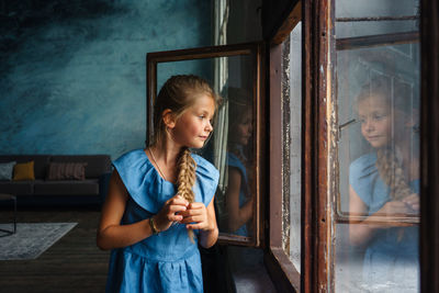 Girl looking away while standing on window