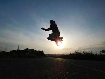 Silhouette man skateboarding on street against sky during sunset