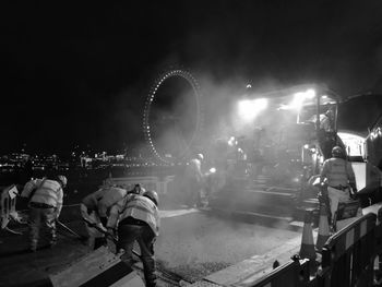 Workers putting asphalt on street with steamroller against millennium wheel