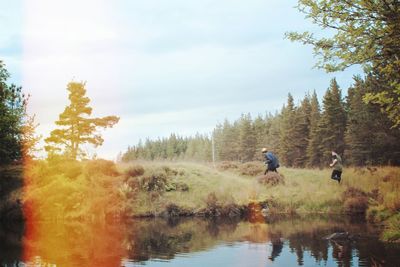 People riding bicycle on riverbank in forest against sky