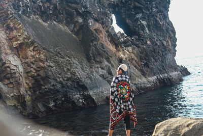 Rear view of person standing on rock by sea