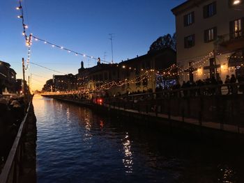 Canal amidst illuminated buildings against sky at dusk