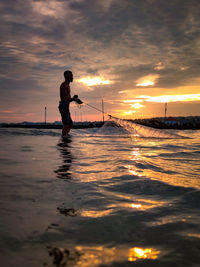 Silhouette man standing on beach against sky during sunset