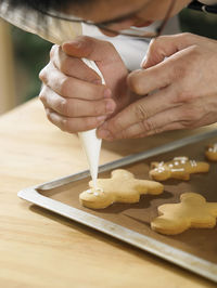 Cropped image of man icing on gingerbread cookies at table