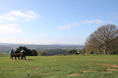 Rear view of people working on agricultural field against sky