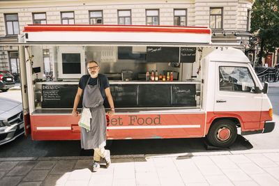 Full length of male chef standing against food truck at city street