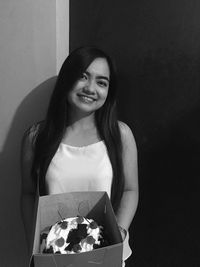 Portrait of smiling young woman with cake standing against wall