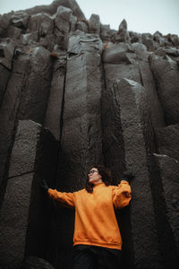 Young tourist in eyeglasses posing near high black stone wall