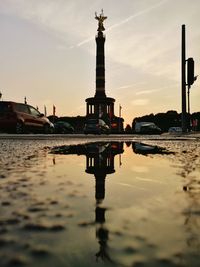 Reflection of victory column on puddle by street during sunset