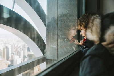 Side view of brothers looking through window at home